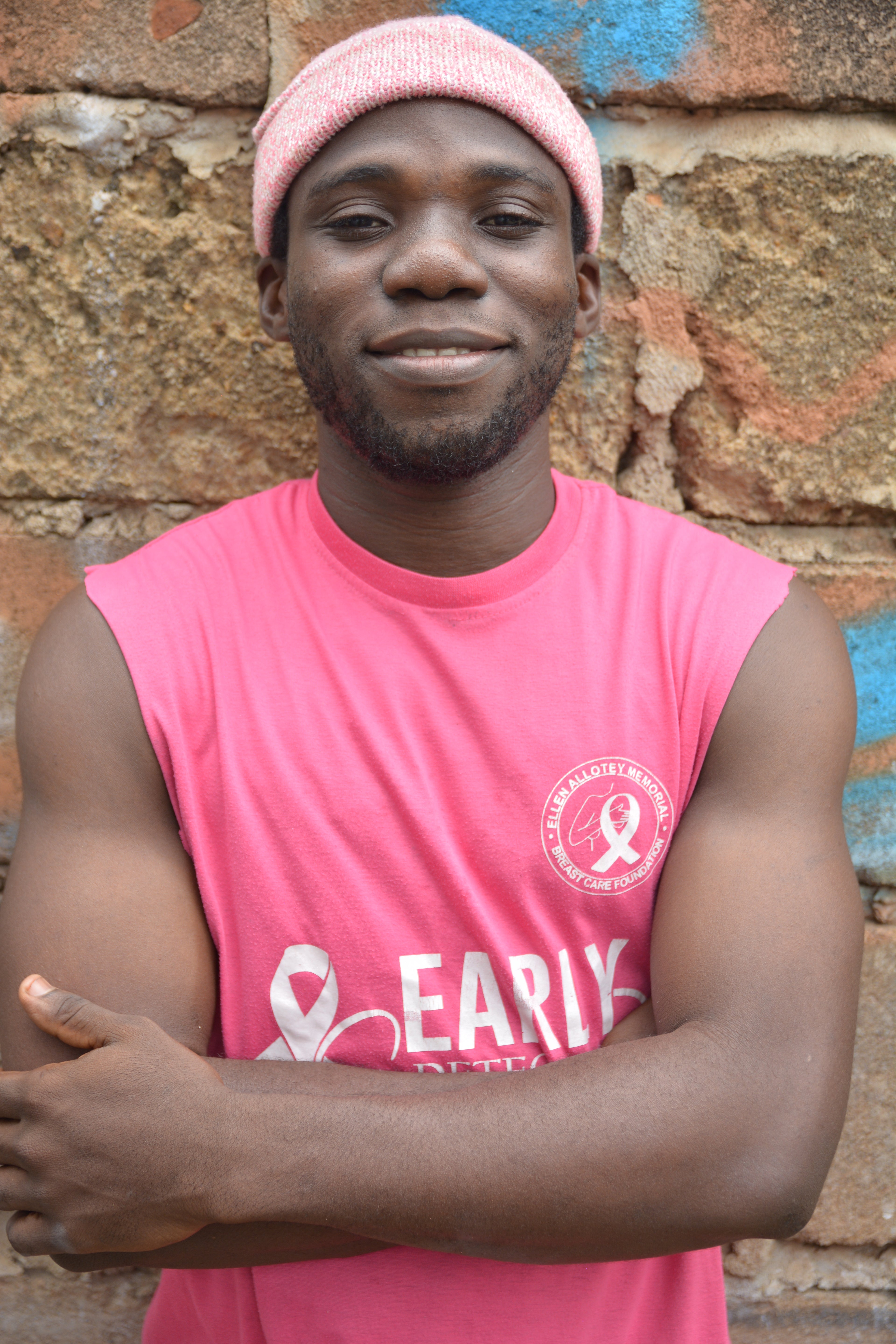 Emmanuel Vifah wearing a pink tank top with visible branding against a textured wall background